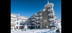 a building with snow on the ground in front of it at Апартамент Bella Casa in Beli Iskar