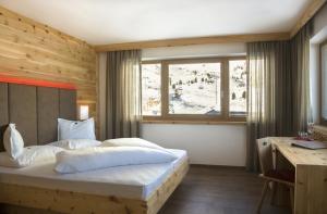 a bedroom with a bed and a desk and a window at Passo Sella Dolomiti Mountain Resort in Selva di Val Gardena +58 photos