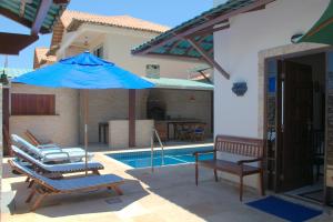 uma piscina com um guarda-sol azul e cadeiras ao lado de uma casa em Pousada Casa do Telhado Verde em Cabo Frio