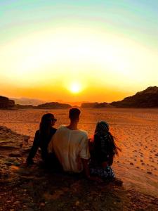 3 Leute sitzen am Strand und beobachten den Sonnenuntergang in der Unterkunft Magic Bedouin Night in Wadi Rum