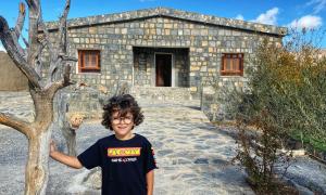 a young boy standing in front of a stone house at Jabal Shams Mountain Rest House in Al Hūb