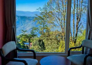 a window with two chairs and a view of the mountains at The Oak Retreat Lamahatta in Darjeeling