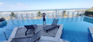 un hombre parado en el balcón de un complejo con la playa en APTO NOVO PÉ NA AREIA - Praia do Sonho, Itanhaém, en Itanhaém
