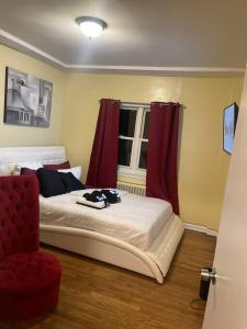 Enhanced 2Bedroom في Williams Bridge: غرفة نوم بسرير مع ستائر حمراء وكرسي احمر