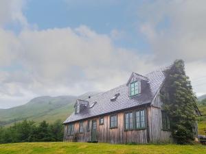a wooden house on a hill with mountains in the background at Loch Long View in Sallachy