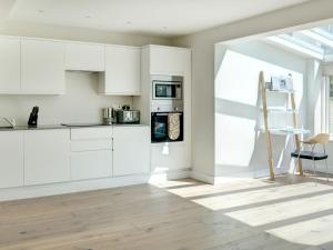 a white kitchen with white cabinets and a chair at Swallows Nest in Bibury