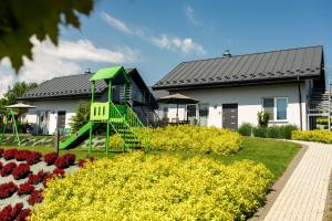uma casa com um parque infantil num jardim com flores em Vela Polańczyk Rodzinne Domki Nad Jeziorem em Polańczyk