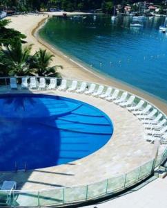 una piscina junto a una playa con sillas y agua en Flat angra, en Angra dos Reis