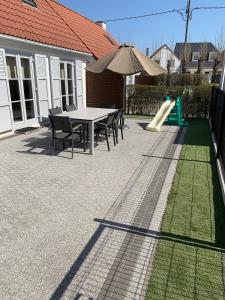 eine Terrasse mit einem Tisch, einer Rutsche und einem Sonnenschirm in der Unterkunft Huisjes aan zee in De Haan