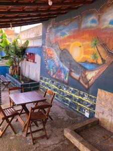 uma mesa e cadeiras em frente a uma parede com um mural em Casa de praia em Figueira, Arraial do Cabo - Casa Caribe em Arraial do Cabo