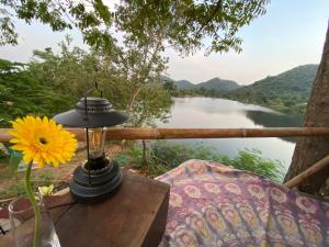 a lamp and a flower on a table with a view of a river at Royal mountain Hut in Ratchaburi