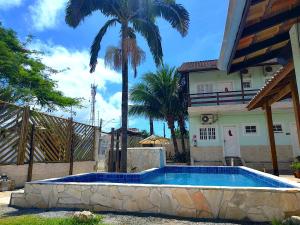 a swimming pool in front of a house with a palm tree at Recanto Maranduba in Ubatuba