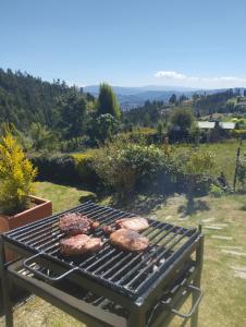 a grill with meat cooking on it in a field at Refugio MALUAN.. Cabaña Villa Nepo in Paipa
