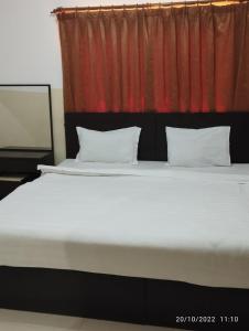 a large bed with two pillows and a red curtain at Al Basateen Hotel Apartment in Sur