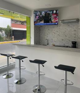 a bar with four stools and a tv on the wall at Hotel Sabana Inn in San José
