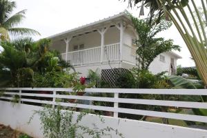 ein Haus mit einem weißen Zaun davor in der Unterkunft Le Colibri et le Frangipanier in La Trinité