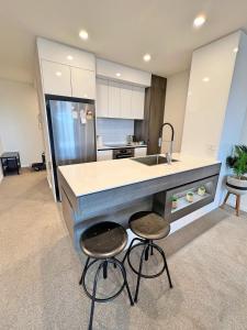 uma cozinha com um balcão e dois bancos e um lavatório em Spacious & Open 2 bd 2bth 2crsp apt - Dickson CBD em Canberra