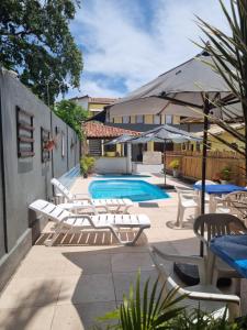 una piscina con tumbonas y mesas blancas y una piscina en Pousada e Restaurante Recanto do Porto, en Porto Seguro
