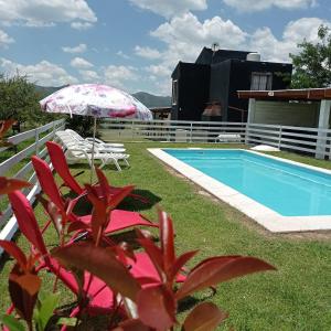 a pool with an umbrella and chairs next to a house at Cabañas Espinillos del Lago in Potrero de Garay