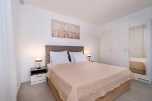 a white bedroom with a large bed and two lamps at House Torre Apartments in Mali Lošinj