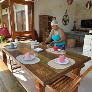 a woman sitting at a wooden table with dishes on it at Vila Gará Kite House - Ilha do Guajiru in Itarema