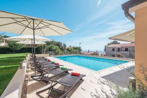 szereg krzeseł i parasol obok basenu w obiekcie E&T apartments with a beautiful pool w Rabacu