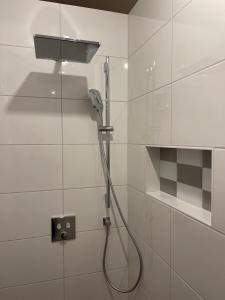 a shower with a hose in a white tiled bathroom at kleines Seeglück in Feldkirchen in Kärnten