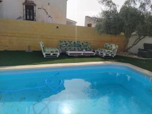 a swimming pool with two chairs and a couch next to a wall at Agradable casa con piscina en la serranía. in Arriate