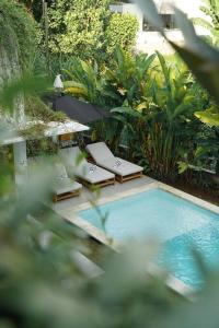 een zwembad met 2 ligstoelen en een parasol bij Villa Ikris - tranquil oasis in the heart of Canggu in Canggu