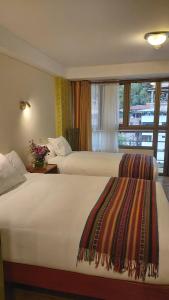 two beds in a hotel room with a window at Hotel Pucara Machupicchu in Machu Picchu