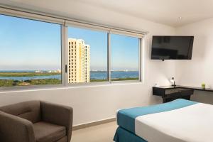 um quarto de hotel com uma cama e uma cadeira e uma janela em Suites Malecon Cancun em Cancún