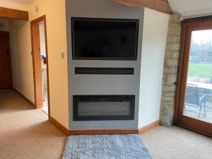 a living room with a fireplace with a flat screen tv at Stable Cottage, Old Mill Farm, Cotswold Water Park in Cirencester
