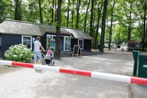 a man walking a child in a stroller in front of a building at Familiecamping De Vossenburcht in IJhorst
