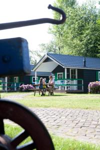 un grupo de personas sentadas en un banco frente a una casa en Familiecamping De Vossenburcht, en IJhorst