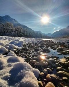 einen schneebedeckten Fluss mit der Sonne im Hintergrund in der Unterkunft Apart-Alpin in Stanzach