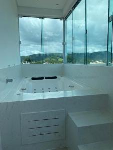 Baño blanco con bañera grande y ventanas en Apartamento Completo com Hidro, en Penha