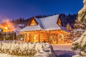 una baita di tronchi nella neve di notte di Chalet Wioska Jagny a Poronin
