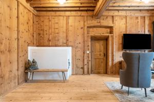 Habitación con paredes de madera, TV y silla. en Alpin Chalet Samer Apt Bauernstube, en Sarentino