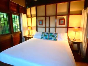 Pacific Edge Eco Lodge في دومينيكال: غرفة نوم بسرير ابيض كبير مع طاولتين
