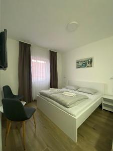 a white bedroom with a bed and a chair at Prenoćište Stari Grad - Old Town in Tuzla