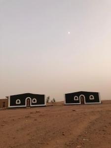 two buildings in the middle of a dirt field at Sahara Authentic Berber Camp in Mhamid