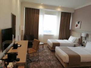 Gloria Hotel & Suites Doha في الدوحة: غرفة فندقية بسريرين ومكتب