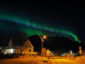 Uma aurora ilumina o céu sobre uma rua em The House of Aurora II em Tromsø