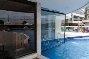 uma vista para uma piscina através de uma janela em 2 QUARTOS a 50m PRAIA dos Anjos em Condomínio Club com PISCINA, estacionamento e portaria 24h - Área de lazer 3000m, wi-fi 450MB, churrasqueira e cozinha completa em Arraial do Cabo
