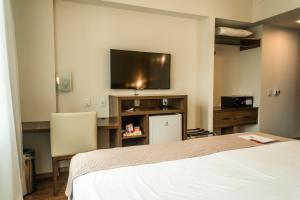 a bedroom with a bed and a flat screen tv at Firenze Business Hotel in Palhoça