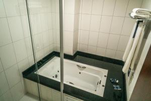 a bath tub in a shower with a glass door at Firenze Business Hotel in Palhoça