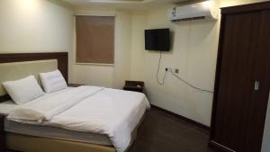 1 dormitorio con 1 cama blanca y TV en la pared en اغصان الريف لشقق المفروشة, en Riad