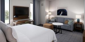 シンシナティにあるStaybridge Suites - Cincinnati East - Milford, an IHG Hotelのベッド、ソファ、テレビが備わるホテルルームです。