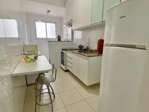 Il comprend une cuisine blanche équipée d'un réfrigérateur et d'une table. dans l'établissement F034 - Apto no Forte Churrasqueira, Wi-Fi e Piscina, à Praia Grande