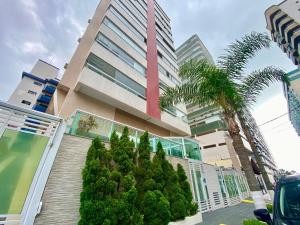 un bâtiment avec des palmiers devant dans l'établissement F034 - Apto no Forte Churrasqueira, Wi-Fi e Piscina, à Praia Grande